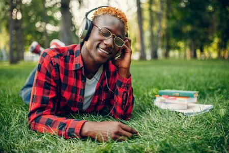 Black student in headphones resting on the grassの写真素材
