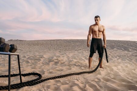 Muscular man doing exercise with rope in desertの写真素材