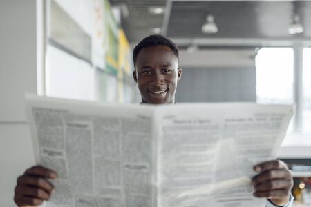 Ebony businessman with newspaper in office hallwayの写真素材