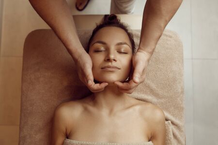 Male masseur hands rubbing face to young womanの写真素材