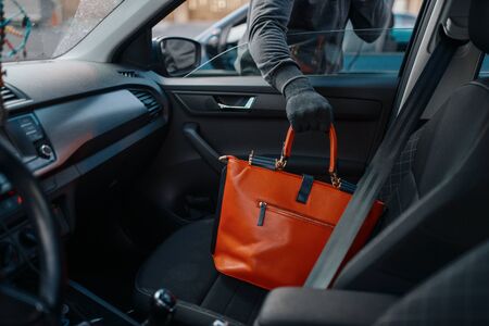Car robber steals women's handbag, criminal lifestyle, stealing. Hooded male bandit opening vehicle...