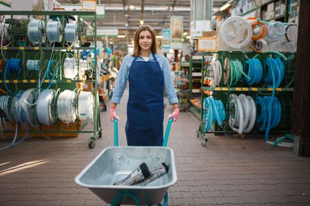 Female seller in apron holds garden cart in shop