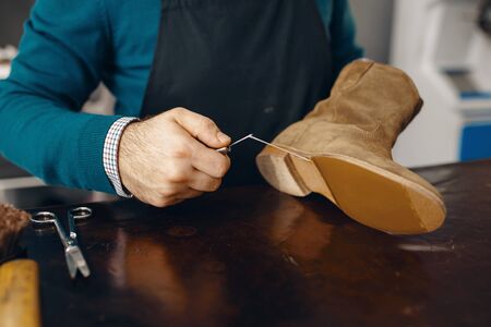 Shoemaker stitches the shoe, footwear repair service. Craftsman skill, shoemaking workshop, cobbler...
