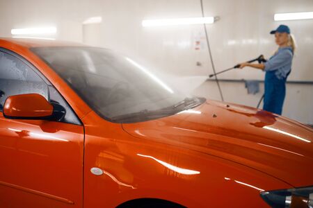 Female washer in uniform poses with high pressure gun in hands, car wash service. Woman cleans vehicle, carwash station, car-wash businessの写真素材