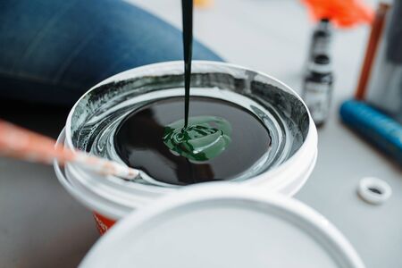 Female house painter mixes black and green paints in pail, closeup. Home repair, laughing woman doing appartment renovation, room decoration renovatingの写真素材