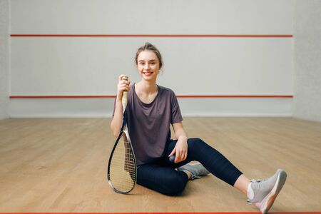 Female player with squash racket sitting on floorの写真素材