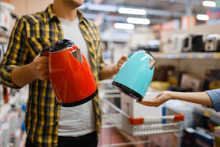 Young couple choosing electric kettle in electronics store. Man and woman buying home electrical appliances in marketの写真素材