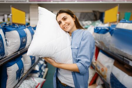 Young woman with pillows in bed linen storeの写真素材