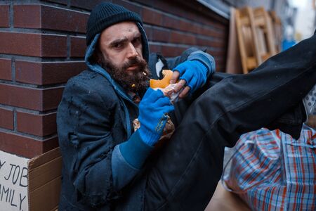 Bearded beggar eats burger on city streetの写真素材