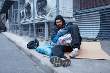 Male bearded beggar lies on city street