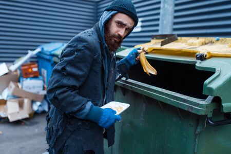 Male bearded beggar searching food in trashcanの写真素材