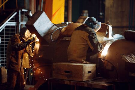 Two welder in masks works with big metal pipe on factory, welding skill. Metalworking industry,...