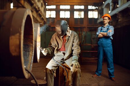 Welder works on factory, worker on background