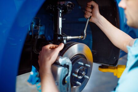 Worker in uniform fix problem on vehicle with removed wheel, car service station. Automobile checking and inspection, professional diagnostics and repairの写真素材