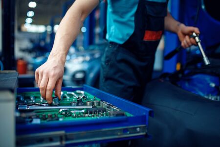 Worker takes wrench from toolbox, car service