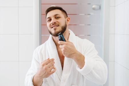 Man shaves his beard with an electric razor