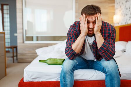 Drunken man awake in bed with bottle of wine