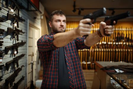 Man aims with two handguns in gun shopの写真素材