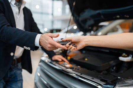 Man and salesgirl choosing auto in car dealership. Customer and seller in vehicle showroom, male...