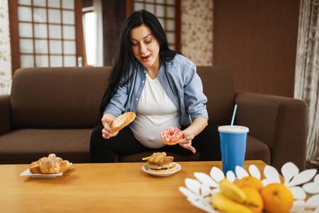 Pregnant woman with belly drinks and eats at homeの写真素材