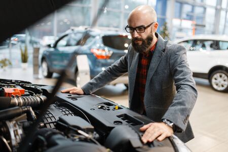 Man poses at new pickup truck with opened hood, car dealership. Customer in vehicle showroom, male person buying transport, auto dealer businessの写真素材