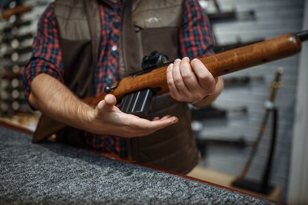 Man loads a rifle at counter in gun shop. Euqipment for hunters on stand in weapon store, hunting and sport shooting hobbyの写真素材