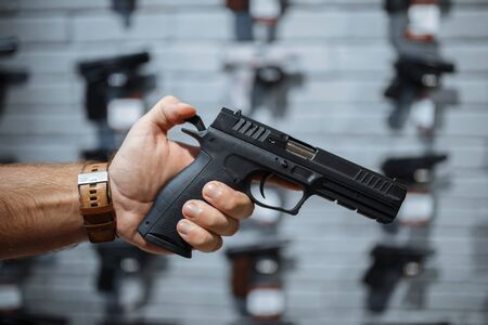 Man choosing new handgun at showcase in gun shop. Male person buying pistol for security in weapon store, selfdefence and sport shooting hobbyの写真素材