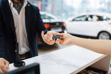 Man takes the key from new auto in car dealership. Customer and saleswoman in vehicle showroom, male person buying transport, automobile dealer businessの写真素材