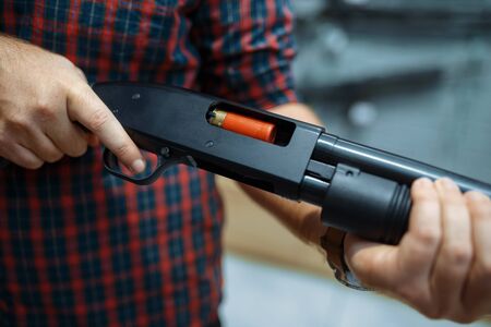 Male person loads rifle at showcase in gun shop. Euqipment for hunters on stand in weapon store, hunting and sport shooting hobbyの写真素材