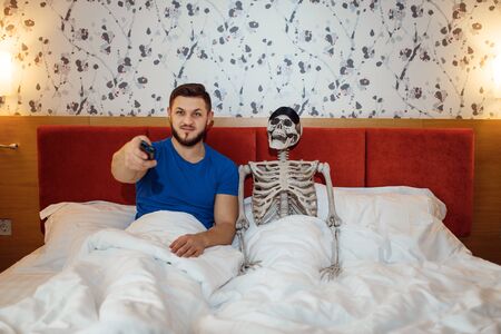 Man and human skeleton watching TV in the bed