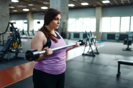 Overweight woman with dumbbells on brench in gym