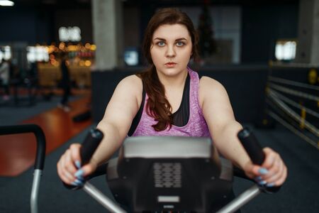 Overweight woman trains on exercise bike in gym