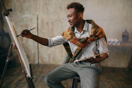 Smiling painter with brush and palette at easelの写真素材