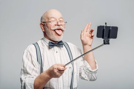 Happy elderly man makes selfie on phoneの写真素材
