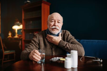 Elderly man takes pills in home officの写真素材