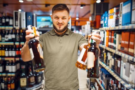Cheerful man choosing alcohol in grocery storeの写真素材
