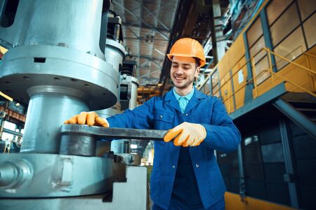 Technician in uniform and helmet works on factory