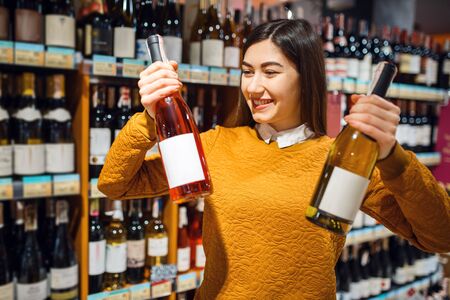 Woman with two bottles of alcohol in grocery storeの写真素材