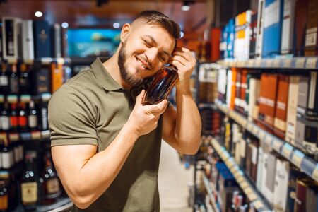 Man hugs bottle of alcohol in grocery storeの写真素材