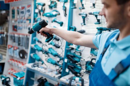 Male worker hand holds electric drill, tool storeの写真素材
