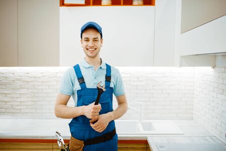 Plumber in uniform fixing faucet in the kitchenの写真素材
