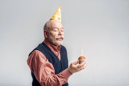 Smiling elderly man in cap shows cake with candle
