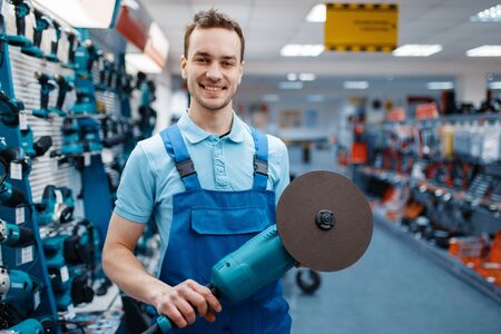 Male worker holds angle grinder in tool storeの写真素材