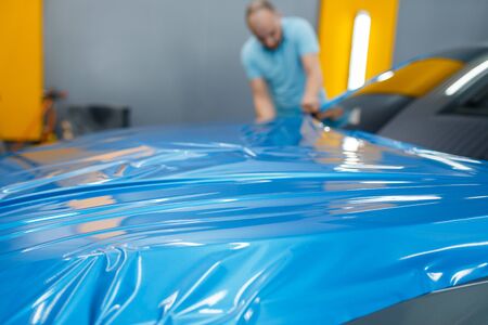 Male car wrapper puts protective vinyl foil or film on hood. Worker makes auto detailing. Automobile paint protection coating, professional tuningの写真素材