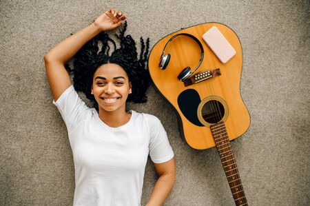 Woman with guitar and headphones lying on floorの写真素材