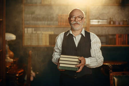Elderly writer holds stack of books in home officeの写真素材