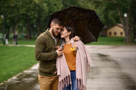 Love couple drinks hot coffee in park, rainy day