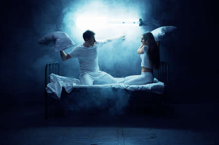 Psycho man and woman fights on pillows in bedの写真素材
