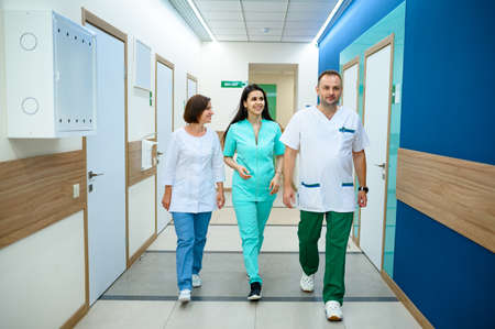 Three smiling doctors walking in clinic corridorの写真素材