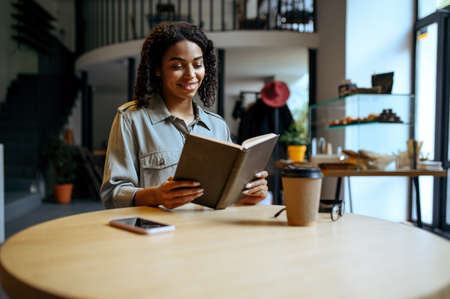 Smiling female student reads a book in cafeの写真素材